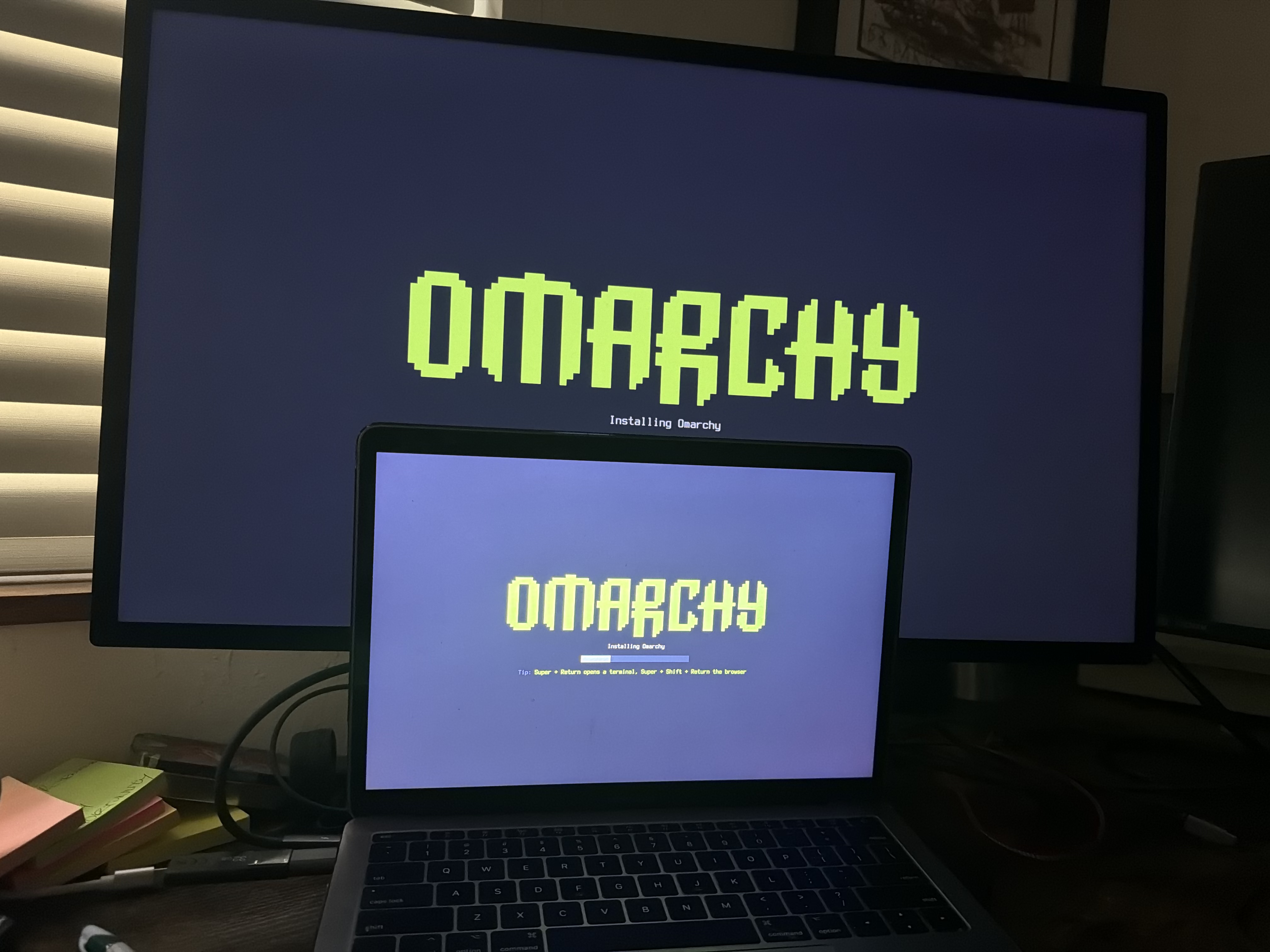Omarchy installing, the progress bar running across both the MacBook's own screen and the external monitor